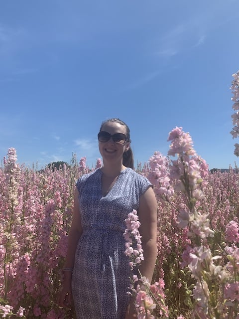 Photo of myself and the pastel pink delphiniums against a clear blue sky